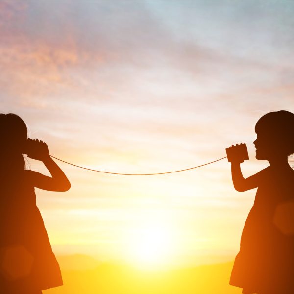 Silhouette of Two female kids stands and talking by using string can phone on beautiful sunset sky